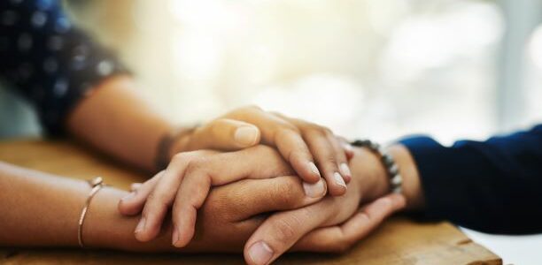 A close up image of a person's hand is clasped between the hands of another person.